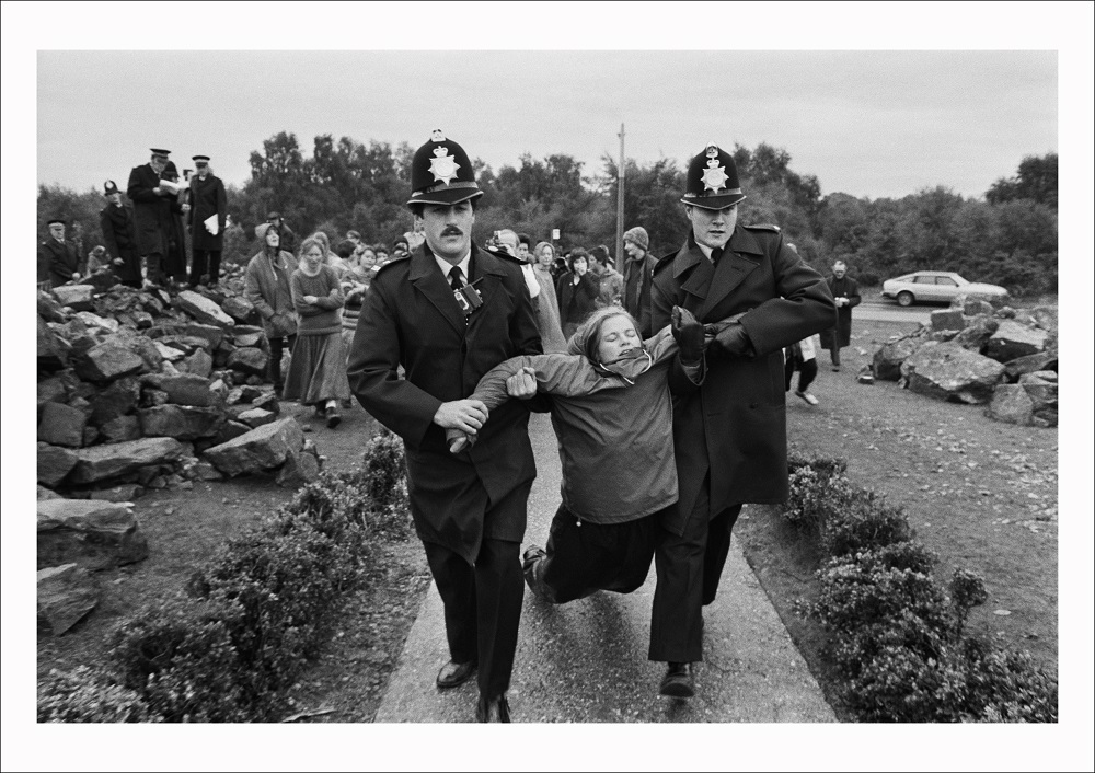A protestor from the Women’s Peace Camp is arrested for obstructing building work outside the Main gate at RAF/USAF Greenham Common, Berkshire (1982)