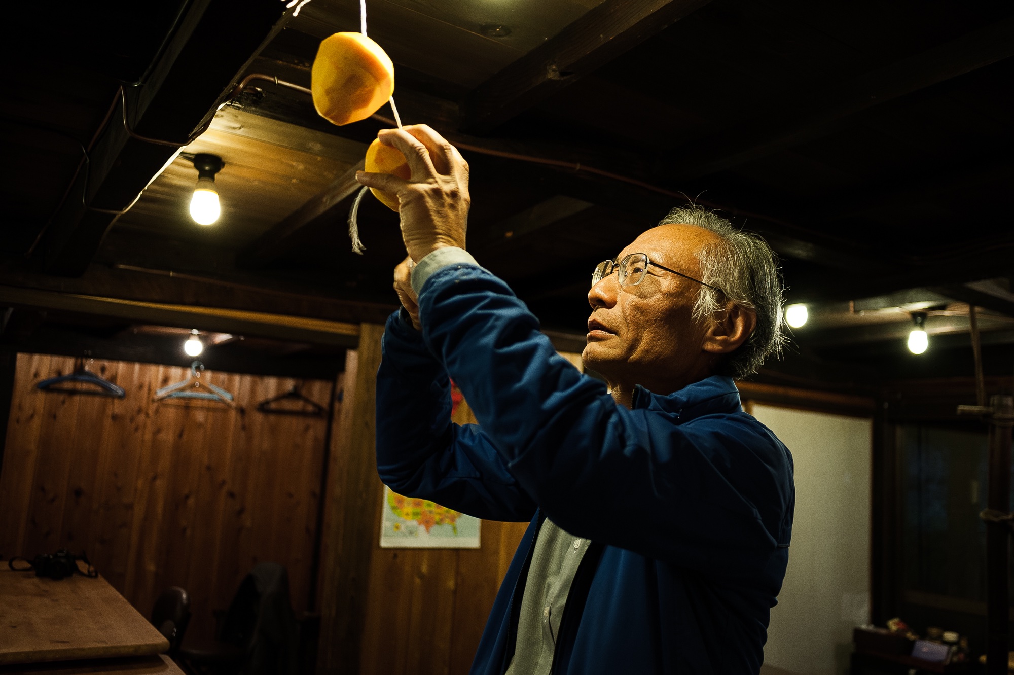 Within the community building, a local man hangs persimmons to dry on string