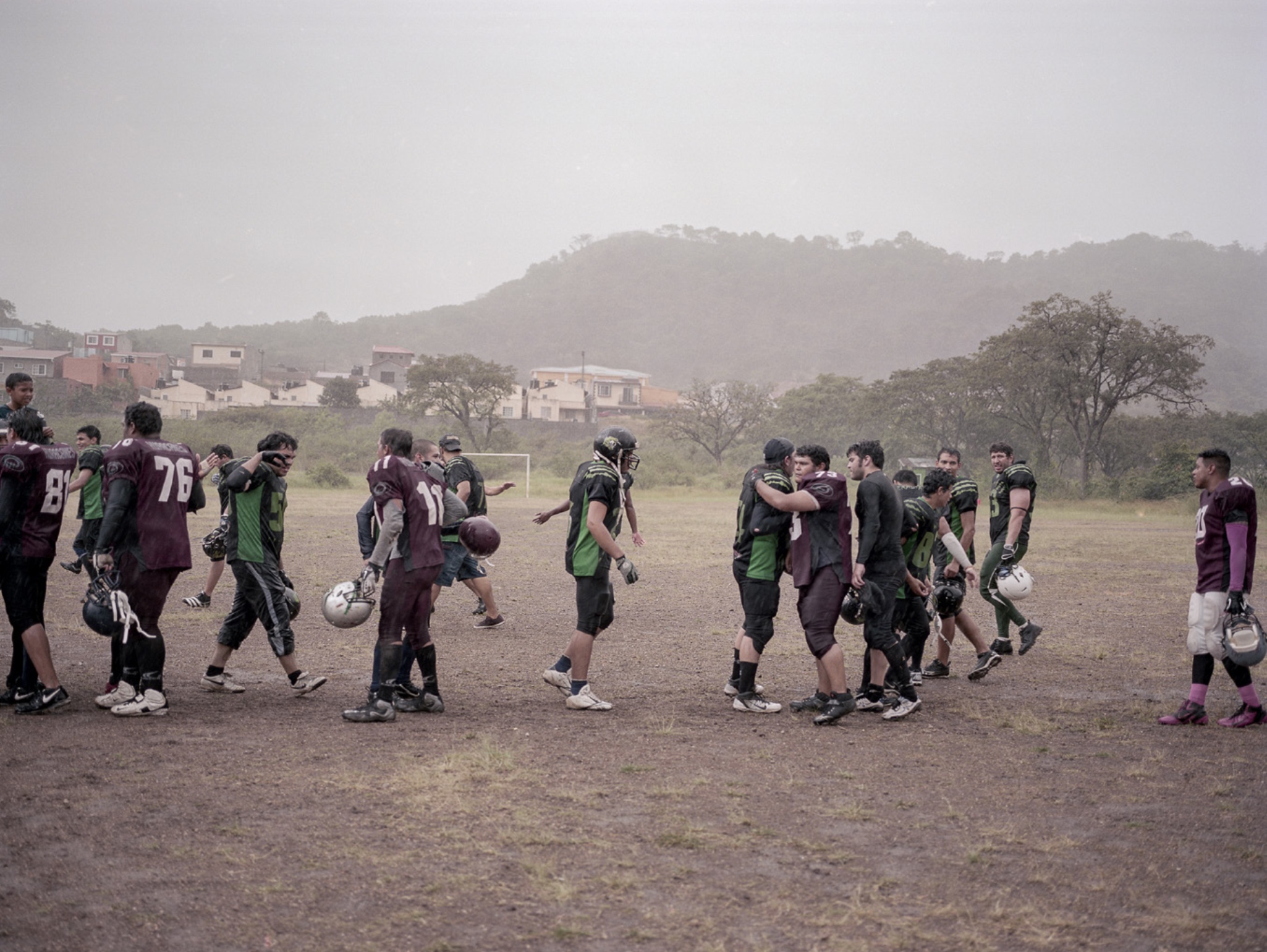 Two teams from the Honduran National American Football League congratulate each other in the rain after a game.