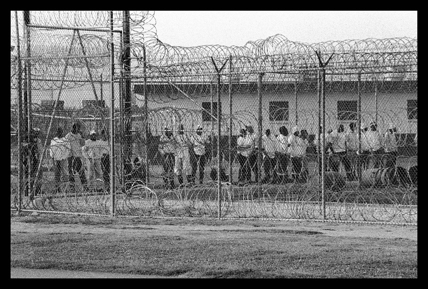 Chandra McCormick. WORK CALL, MEN BEHIND BARBED WIRE FENCING WAITING TO GO TO WORK IN THE FIELDS OF ANGOLA, 2004.