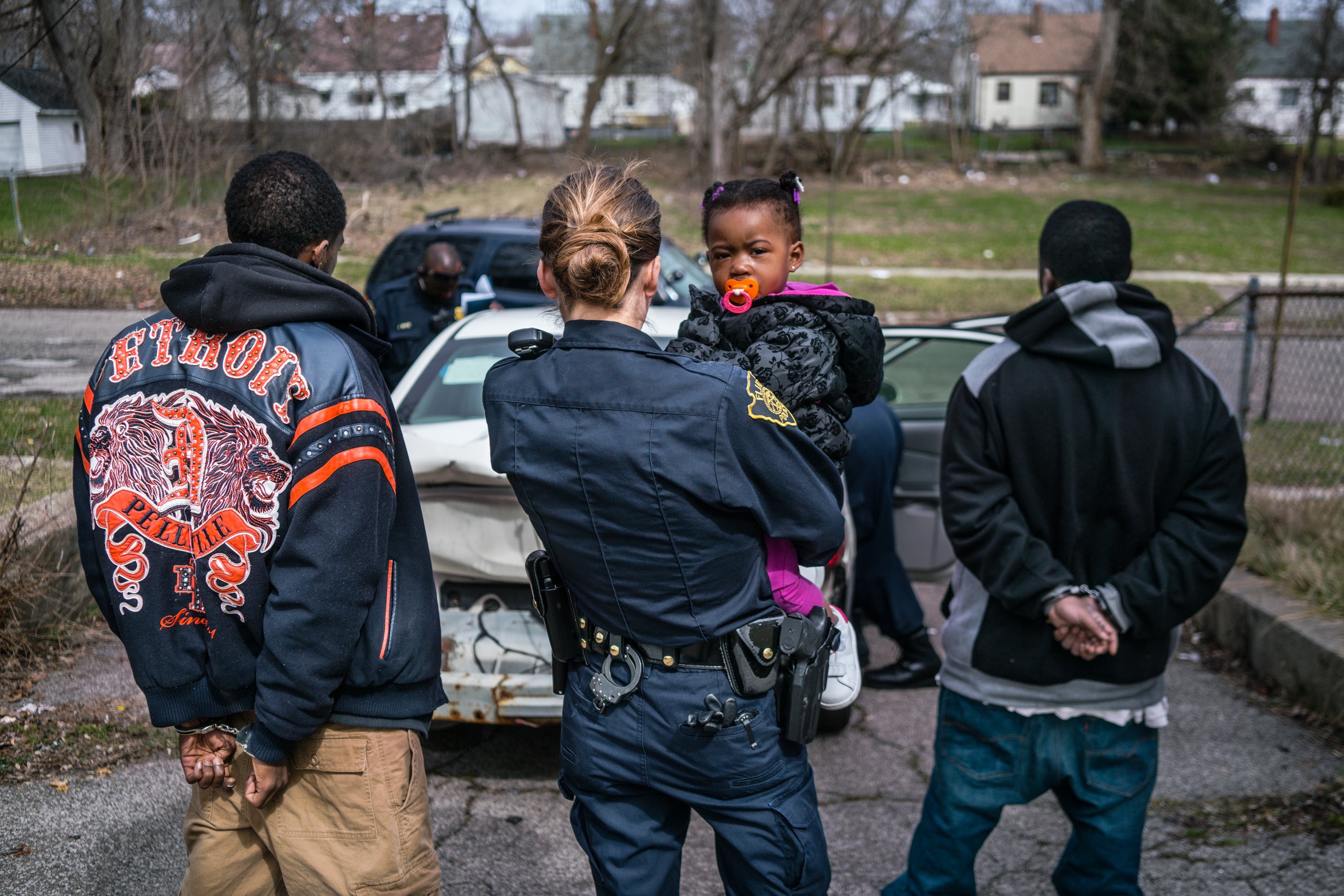 Officer Bridget Balasko holds a small child while her father is being searched and questioned. March, 2016.