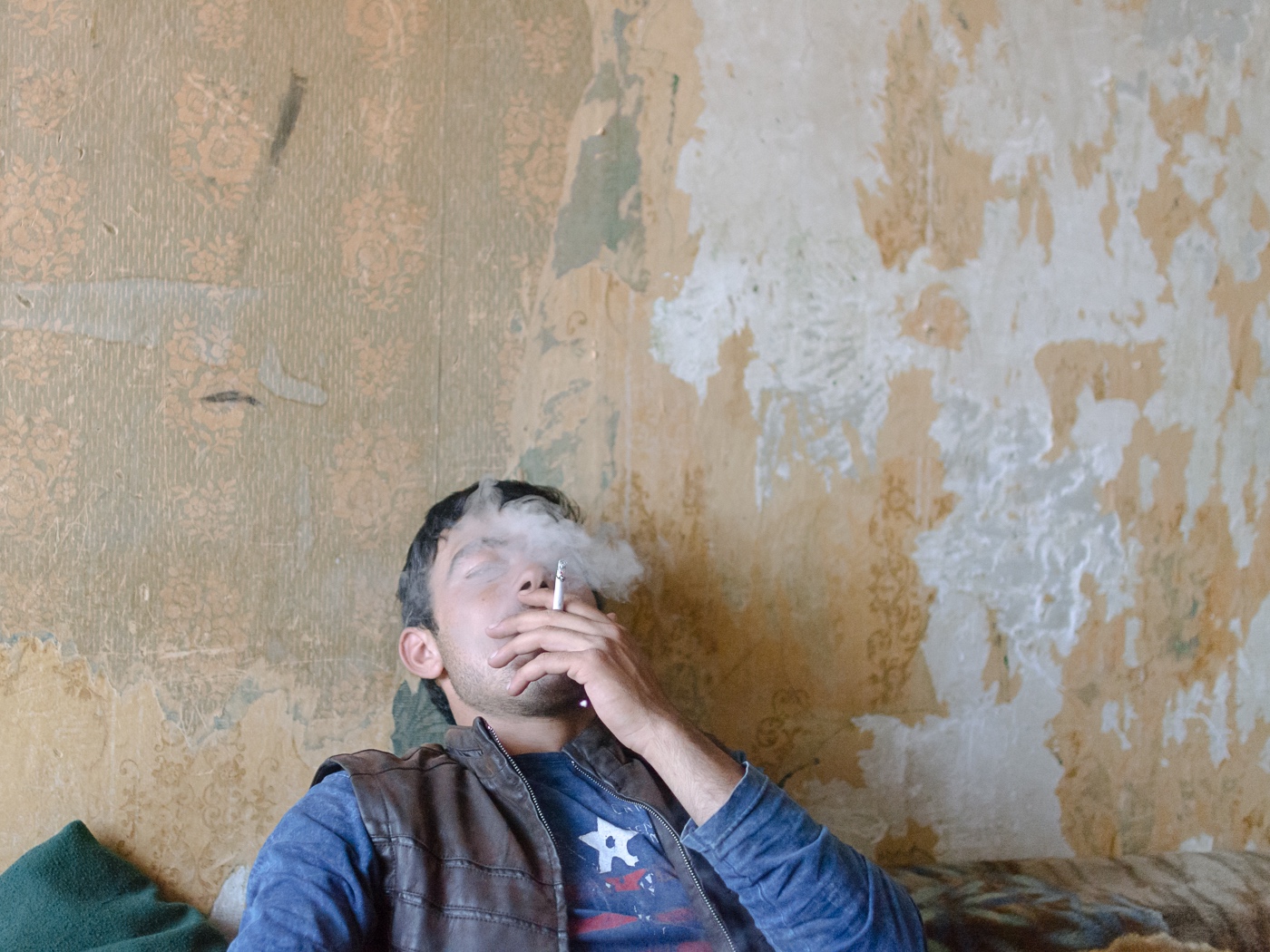 A friend of Edo smokes a cigarette in Edo's room. Just like this one, most apartments are furnished sporadically. Their owners are in lack of any means to renovate their homes.